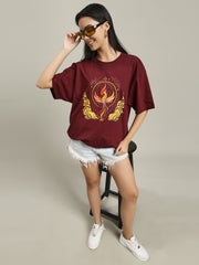 Woman standing and smiling, wearing a maroon Fire women's over-sized T-shirt with a phoenix fire print on the front, paired with white distressed shorts and white sneakers, posing against a neutral background