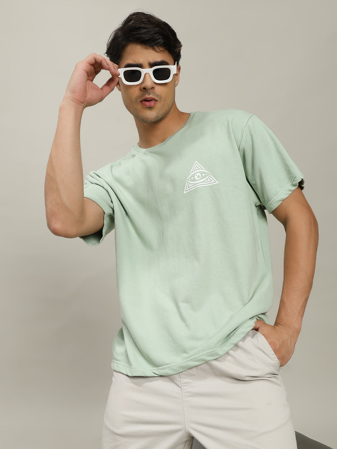 Man wearing a light green t-shirt with a logo and white sunglasses against a plain background