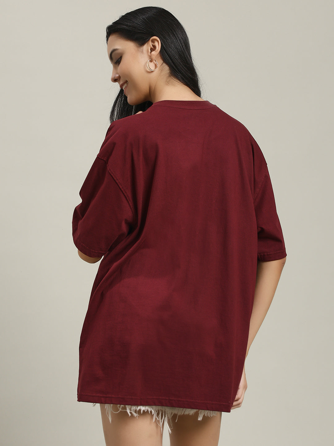Woman wearing a maroon Fire women's over-sized T-shirt with a phoenix and fire design on the front, facing away from the camera, showing the loose fit and shoulder seam details
