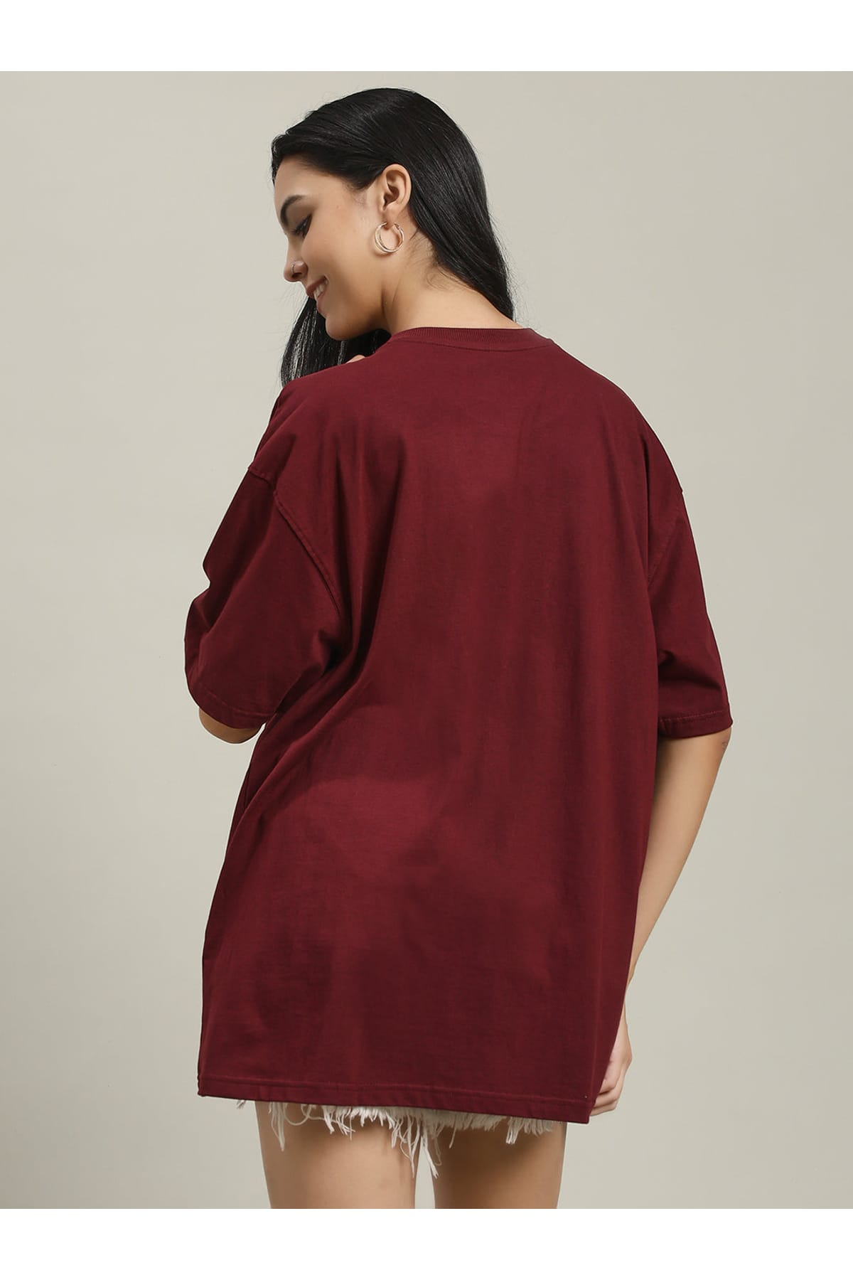 Woman wearing a maroon Fire women's over-sized T-shirt with a phoenix and fire design on the front, facing away from the camera, showing the loose fit and shoulder seam details