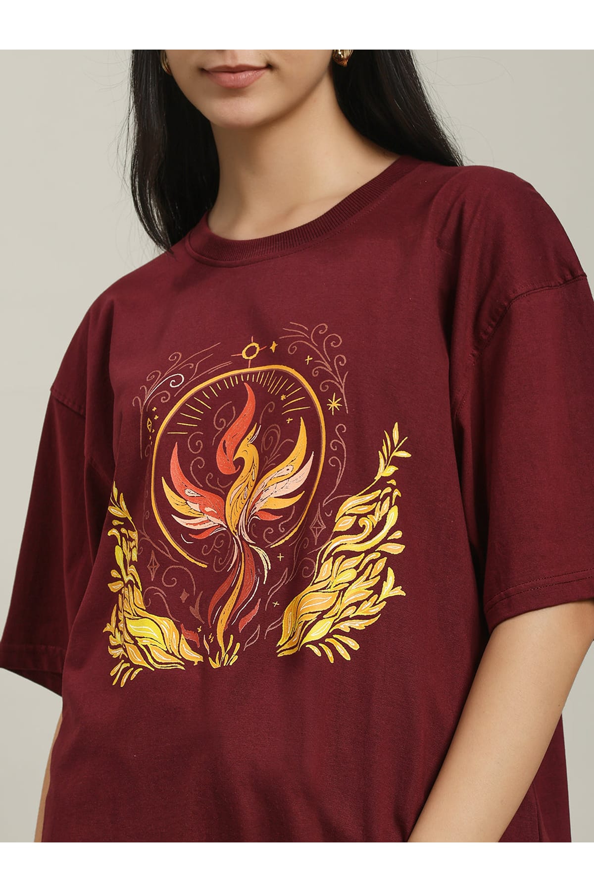 Detailed close-up of the Fire women's over-sized T-shirt featuring a vibrant phoenix surrounded by flames and ornate golden leaves, highlighting the intricate design and rich maroon fabric